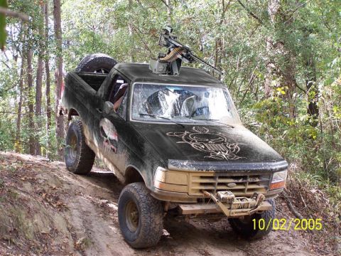 1993 Ford Bronco - Modified 1993 Ford Bronco equipped with a machine gun and off-road tires navigates a dirt trail.
