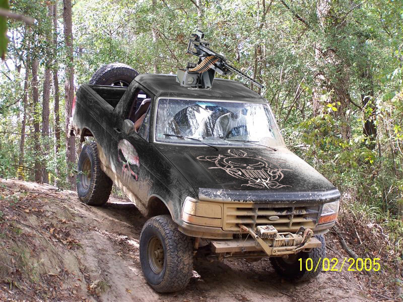 Black muddy lifted Ford Bronco on dirt off-road trail with front winch and roof-mounted gun prop