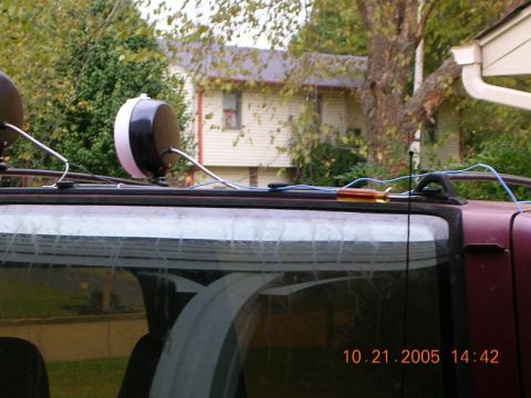 1989 Ford Bronco II - A close-up view of a vehicle's roof, showing aftermarket lights and exposed wiring, with a house visible in the background.