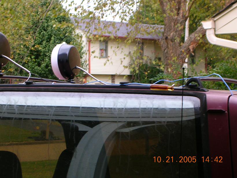 Car roof with two lights, wiring, and a screwdriver on top. House in background