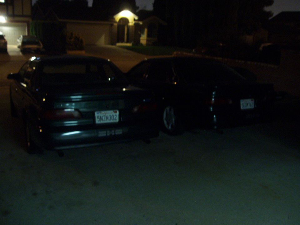 1995 Ford Taurus and another sedan parked in a driveway at night. License plate 5NZH302 is visible