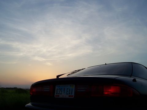 1994 Ford Probe - The rear of a dark car is visible against a sunset sky, with a license plate in view.