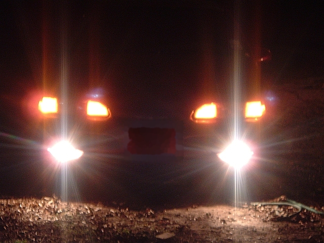 Front of a vehicle at night with glowing headlights and amber turn signals