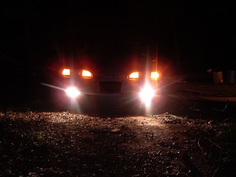 1994 Ford Thunderbird - The front of a car is illuminated by its headlights at night, with the ground covered in leaves and debris.