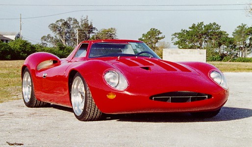 Red sports car with a low profile, rounded body, and prominent hood vents, viewed from a 3/4 front angle