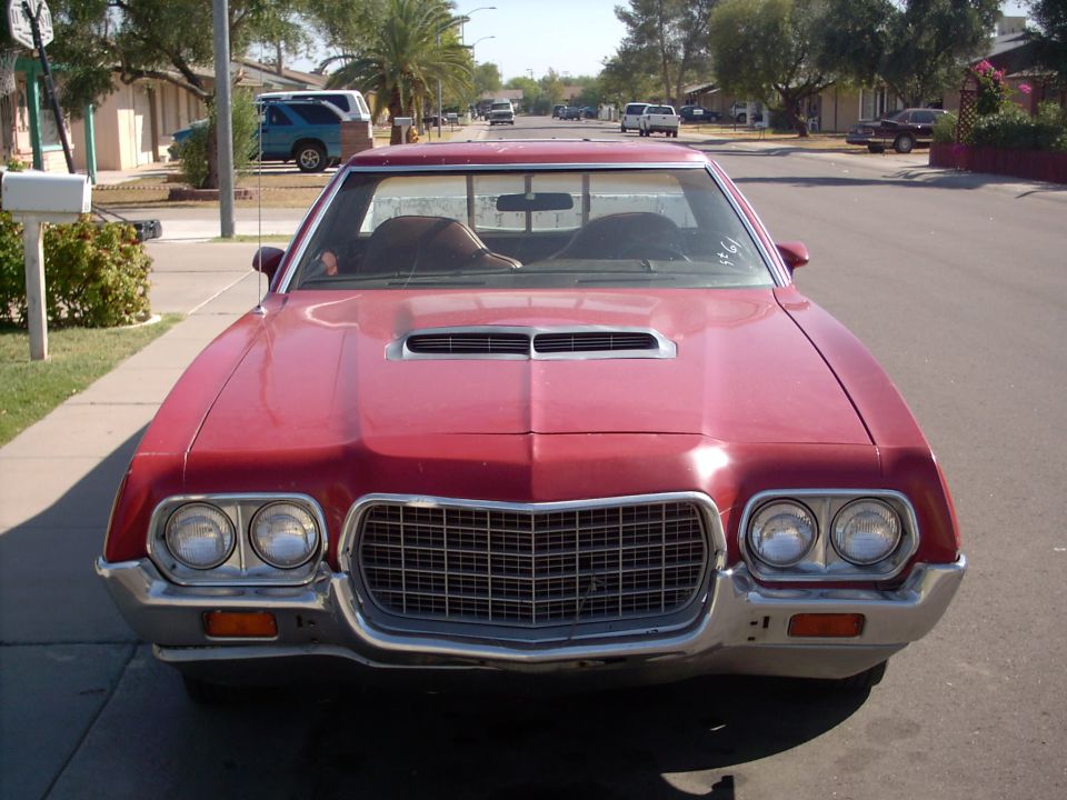 Dark red 1972 Ford, front view, dual headlights and chrome grille on a suburban street