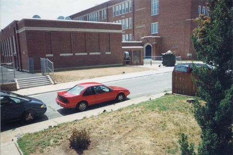 1996 Chevrolet Beretta - A red 1996 Chevrolet Beretta coupe is parked on the street in front of a brick building.