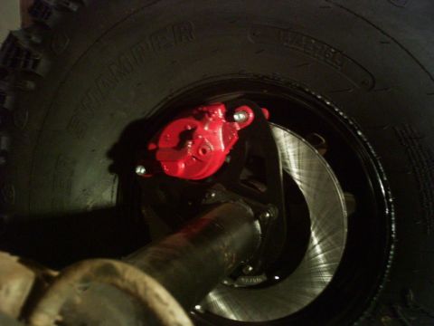 1986 Ford Bronco - Close-up view of a red brake caliper and rotor assembly, likely part of a vehicle's braking system.