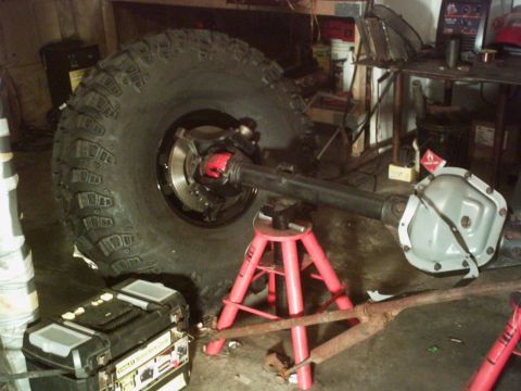 1986 Ford Bronco - A Dana 60 axle assembly, a large off-road tire and brake components, is supported by red jack stands in a workshop.