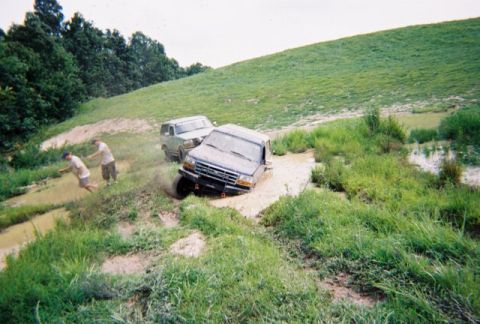 1995 Ford Bronco - Two SUVs navigate a muddy terrain, with one vehicle deeply entrenched in the mire while others observe.