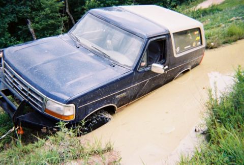 1995 Ford Bronco - A dark blue Ford Bronco with a beige top is stuck in a muddy ditch.