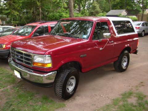 1995 Ford Bronco - A red Ford Bronco is parked outdoors next to other vehicles.