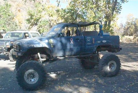 1986 Ford Bronco - A heavily modified blue truck with oversized tires is parked on a dirt surface, with another vehicle visible behind it.
