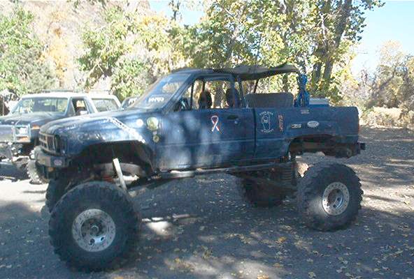 Blue lifted off-road truck with large tires, soft top, and various decals, parked outdoors
