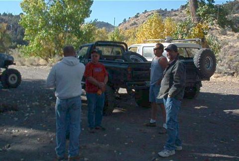 1986 Ford Bronco - Four men gather around a black pickup truck parked outdoors, with a spare tire visible on the rear.