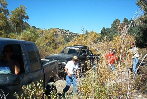 1986 Ford Bronco - Two pickup trucks are parked in a dry, brushy landscape with people around them.