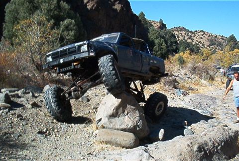 1986 Ford Bronco - A heavily modified truck navigates a rocky trail with other vehicles in the background.