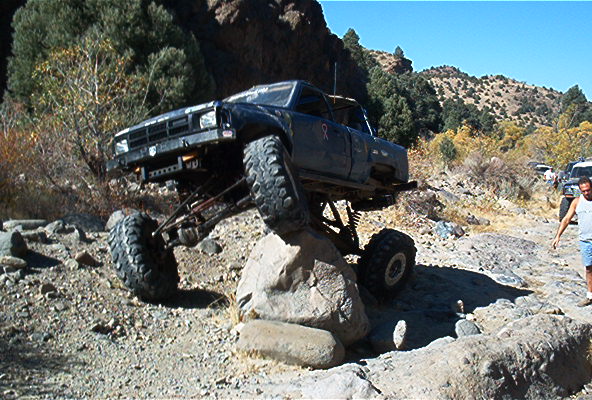 Dark gray lifted mini-truck on oversized mud tires flexing over a boulder on a desert trail