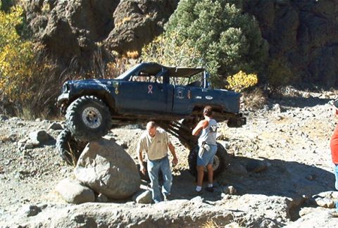 1986 Ford Bronco - An off-road vehicle is shown traversing a challenging rocky landscape with two people observing.