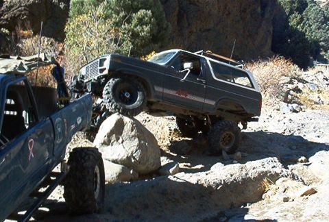 1986 Ford Bronco - Two off-road vehicles navigate a rocky trail in a canyon setting.