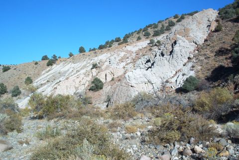 1986 Ford Bronco - A view of a rocky hillside with sparse vegetation under a clear blue sky. The image contains a watermark for SuperMotors.net.
