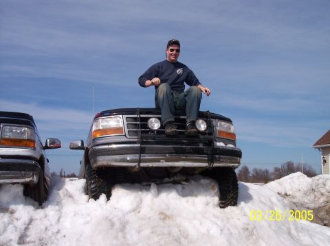 1995 Ford Bronco - Two Ford Broncos are stuck in snow, one with a man sitting on its hood.