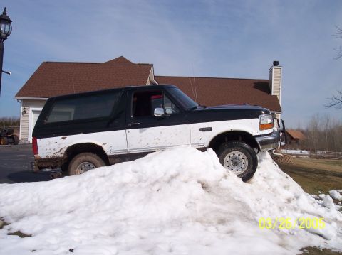 1995 Ford Bronco - A white and black 1995 Ford Bronco navigates a large snow pile on a sunny day.