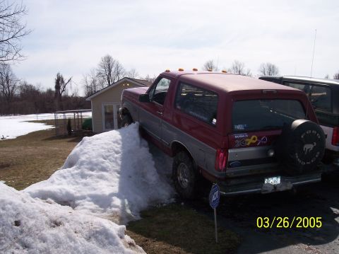 1995 Ford Bronco - A red and silver 1995 Ford Bronco is partially on a snow pile with a second vehicle visible to the right.