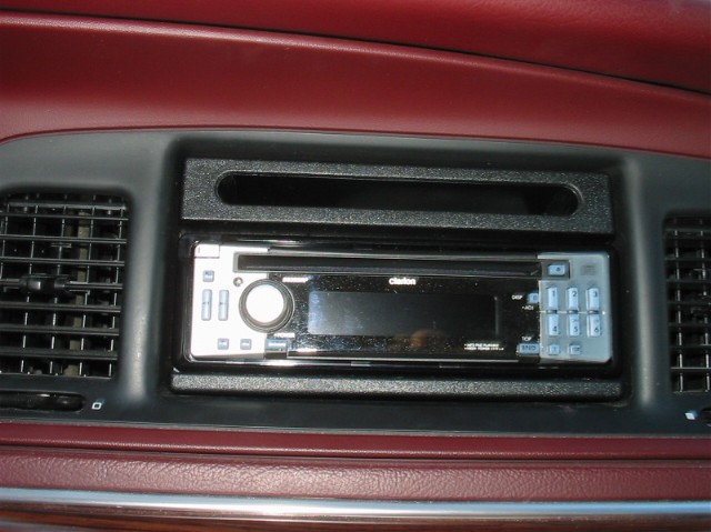 Car dashboard with Clarion stereo and air vents. Red interior trim visible