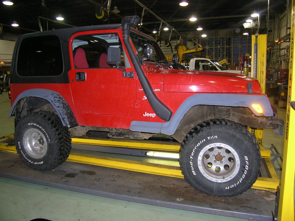 Red Jeep TJ on a lift, has a snorkel and aftermarket wheels