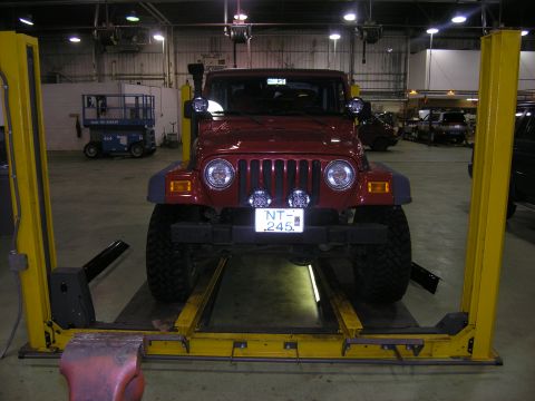 2001 Jeep Wrangler - A red Jeep TJ is positioned on a car lift in a garage, showing its front grille and license plate.