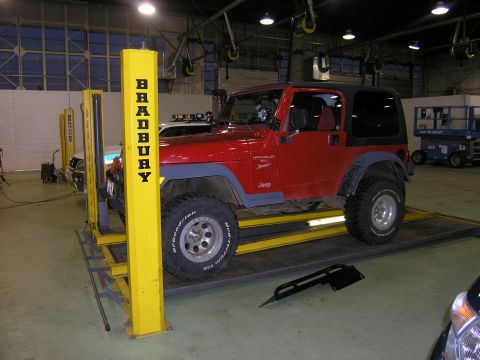 2001 Jeep Wrangler - A red 2001 Jeep TJ Wrangler is positioned on a Bradbury lift, likely for service or inspection.