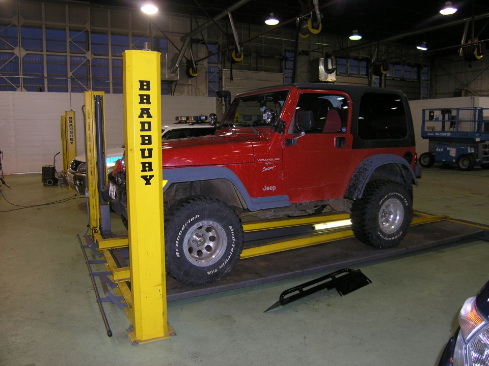Red 2001 Jeep TJ Wrangler on a lift with 'BRADBURY' lift posts