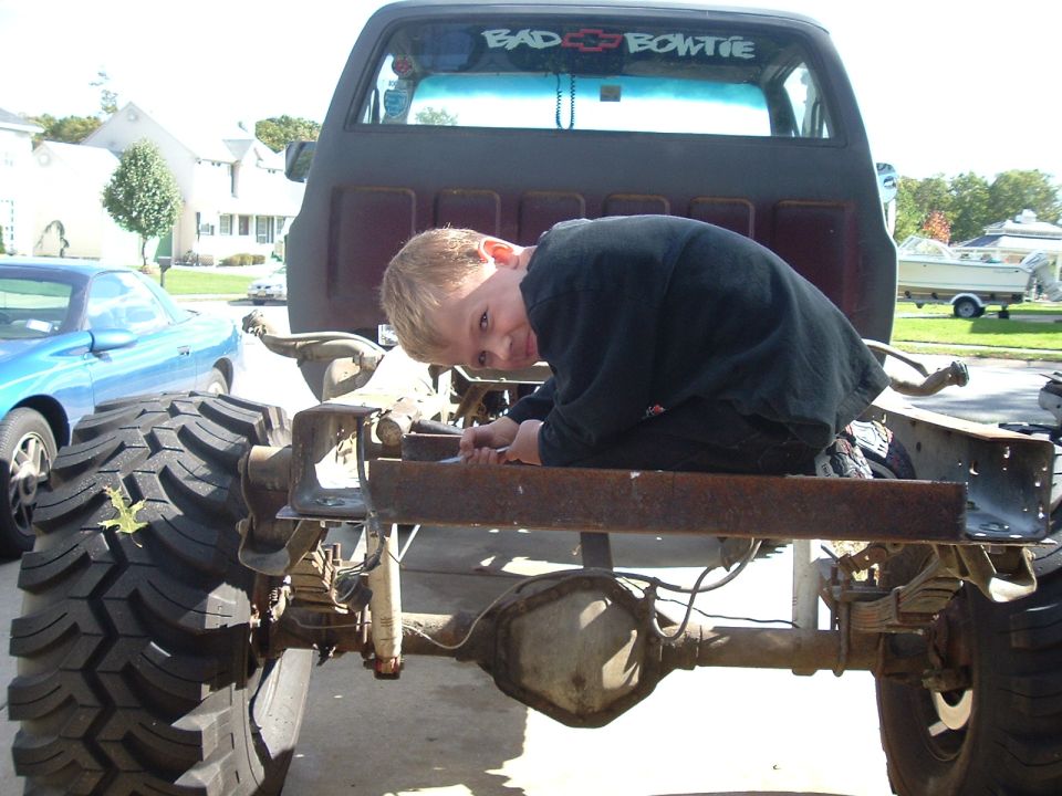 Boy leaning on the bare rear frame of a lifted square-body Chevy pickup
