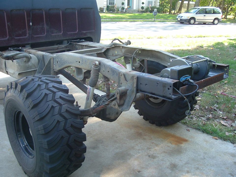 Bare pickup frame with rear-mounted winch on crossmember, leaf springs, shocks and mud tires
