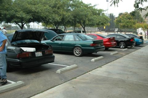 1991 Ford Taurus - Several cars are parked in a lot, including a green sedan with its trunk open.