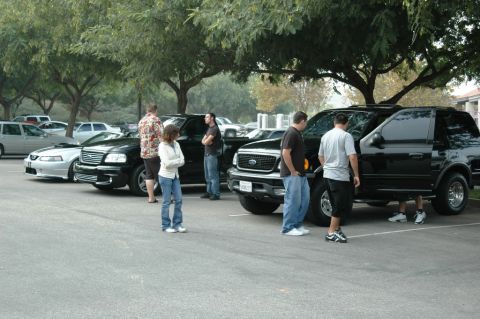 1991 Ford Taurus - Several SUVs are parked in a lot with people standing around them.