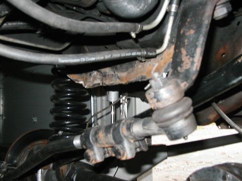 1994 Ford Bronco - Detail of vehicle suspension and undercarriage components, including a rusty frame section and a transmission oil cooler hose.