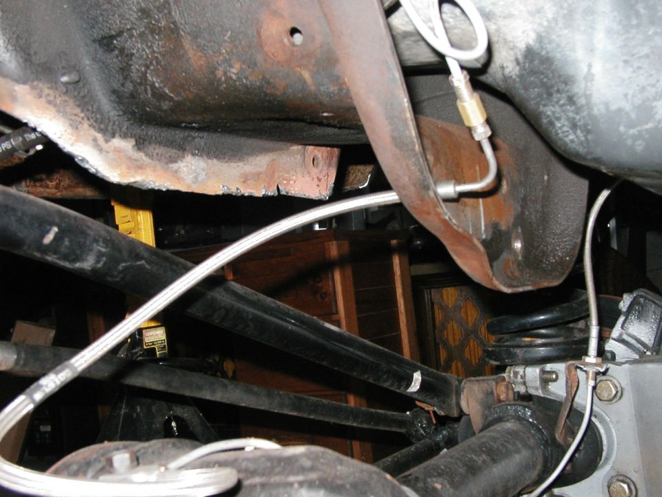 Underside of a vehicle showing rusty frame, suspension components, and brake lines