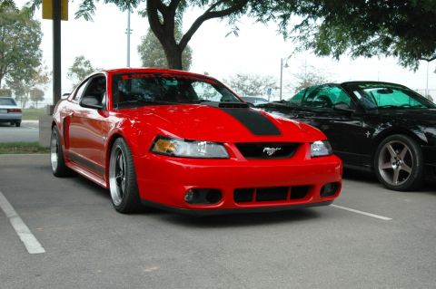 1991 Ford Taurus - A red Ford Mustang is parked in a lot next to a black convertible.
