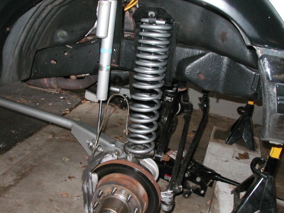 Front suspension components including coil spring, shock absorber, brake rotor, and steering linkage, with jack stands supporting the frame