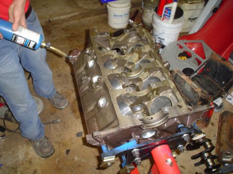 1981 Ford Bronco - A person uses a torch to work on an engine block that is mounted on a stand, with various parts and containers in the background.