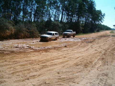 1991 Ford Bronco - A 1991 Ford Bronco struggles through a muddy track, with a pickup truck following close behind.
