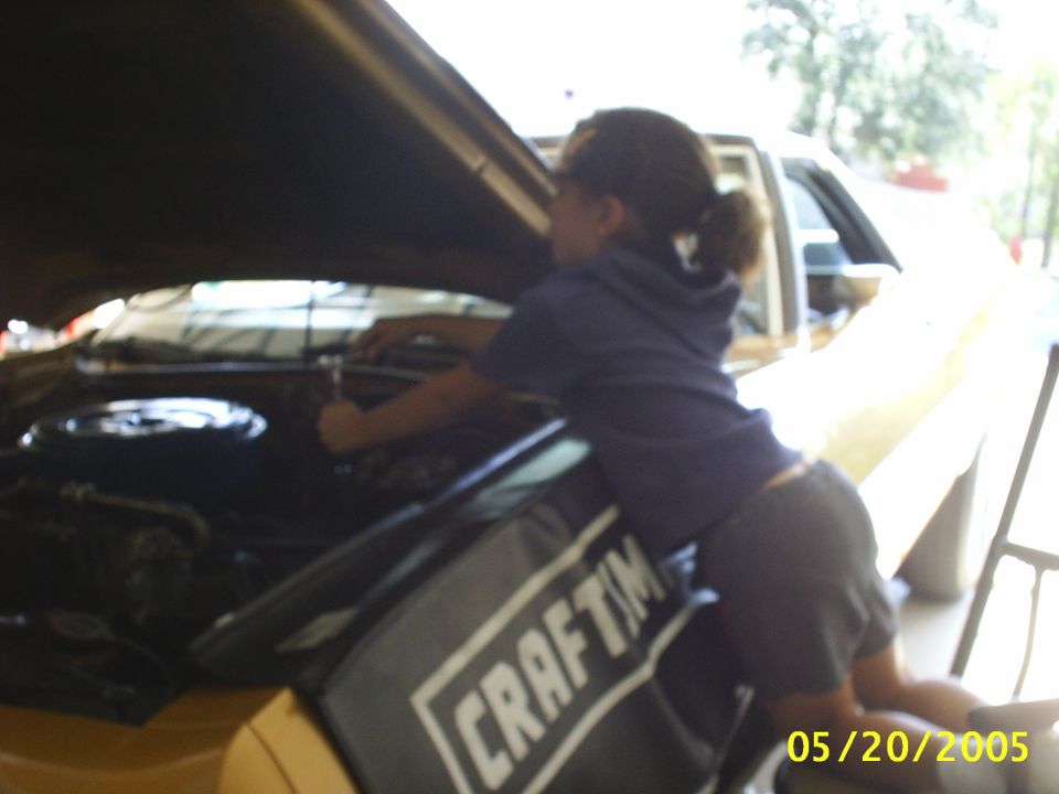 Child leaning over a Craftsman fender cover into the engine bay of a yellow car with hood raised