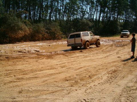 1991 Ford Bronco - 1991 Ford Bronco navigates a muddy off-road course with another vehicle visible.