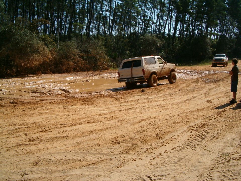 1991 Ford Bronco driving through mud pit, another truck in background