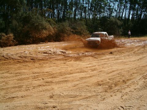 1991 Ford Bronco - A white pickup truck navigates a challenging muddy terrain, creating a large splash.