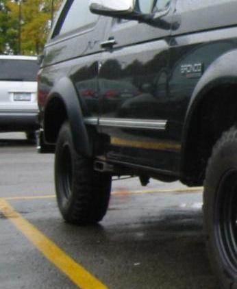 1995 Ford Bronco - A black 1995 Ford Bronco is viewed from the side, with a white SUV in the background.
