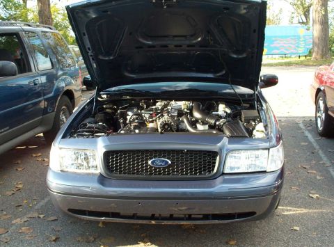 1998 Ford Crown Victoria - Front view of a 1998 Ford Crown Victoria's engine bay, parked outdoors with other vehicles nearby.