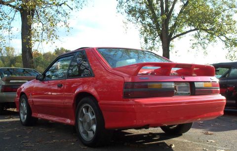 1998 Ford Crown Victoria - Rear view of a red coupe with a spoiler, parked outdoors with trees in the background.
